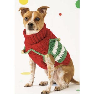 May include: A small brown and white dog wearing a red crocheted sweater with a high ribbed collar. The sweater features green trim, white and green striped side panels, and three small gold-colored jingle bells attached to the edges.