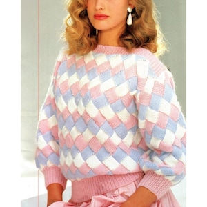 Könnte beinhalten: Ein pastellfarbener Pullover mit einem gewebten Muster in Rosa, Weiß und Hellblau. Der Pullover hat einen Rundhalsausschnitt, lange Ärmel und gerippte Bündchen und Saum. Das Design erzeugt einen Schachbretteffekt.