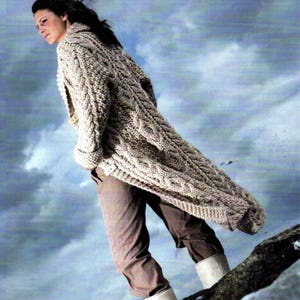 May include: A long, beige, cable-knit cardigan featuring a thick, textured wool pattern with prominent vertical braids. The garment has long sleeves, a folded collar, and a button-front closure, extending down to the mid-thigh area.