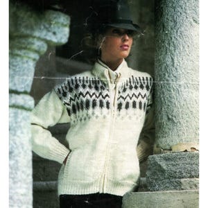 Könnte beinhalten: Cremefarbener Reißverschluss-Pullover mit einem schwarz-grauen geometrischen Muster auf Brust und Schultern. Der Pullover hat einen hohen Kragen und lange Ärmel. Das Model trägt einen schwarzen Hut.