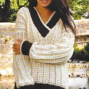 May include: Cream-coloured, long-sleeved sweater with a deep V-neck and dark brown trim. The sweater features a textured knit design with openwork details on the sleeves and body. The cuffs and hem are also dark brown.