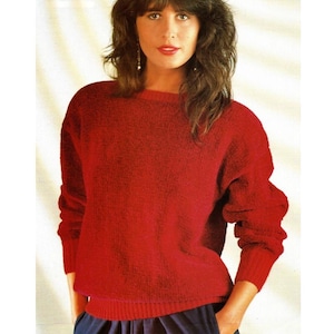 May include: A red knit sweater with a crew neck and long sleeves. The sweater has a ribbed hem and cuffs. The person in the image is wearing the sweater with blue pants. The sweater appears to be made of a soft, textured material.