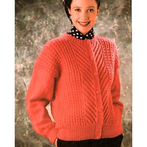 May include: A bright coral-colored knit cardigan featuring a textured cable-knit pattern on the front and sleeves. The garment has a round neckline, long sleeves, and a front button closure with matching coral buttons, worn over a black polka-dot shirt.