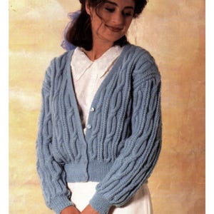 May include: A light blue cable-knit cardigan featuring a V-neckline, long sleeves, and a button-front closure. The garment is worn over a white collared shirt. The knit pattern consists of vertical cable textures throughout the body and sleeves.