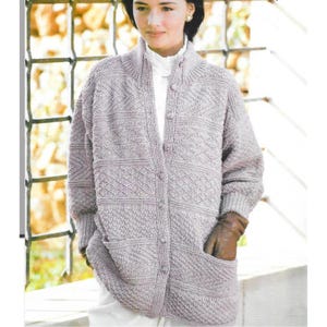 May include: A light gray, long-sleeved cardigan with a textured knit pattern. The cardigan has a button-up front, a high collar, and two front pockets. The sleeves have ribbed cuffs. The person is wearing brown gloves.
