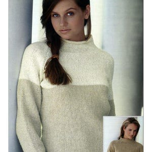 Könnte beinhalten: Ein cremefarbener und beigefarbener Strickpullover mit Stehkragen. Der Pullover hat lange Ärmel und ein horizontales Farbblockdesign über der Brust. Das Model trägt den Pullover und hat lange braune Haare.