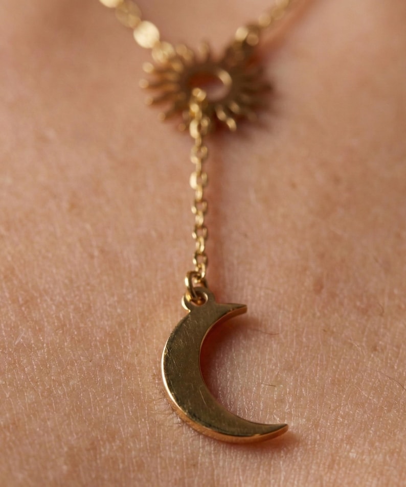May include: Gold-colored necklace featuring a sunburst pendant and a crescent moon charm. The necklace has a delicate chain and is designed to be worn around the neck. The sunburst pendant is at the top, with the moon charm hanging below.