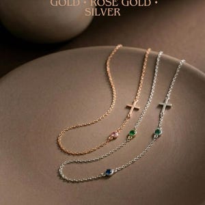 Puede incluir: Tres delicados collares con colgantes de cruz y detalles de piedras preciosas en oro, oro rosa y plata. Cada collar presenta una peque&ntilde;a gema rosa, verde o azul. El texto dice: "CHOOSE YOUR COLOR GOLD &bull; ROSE GOLD &bull; SILVER."