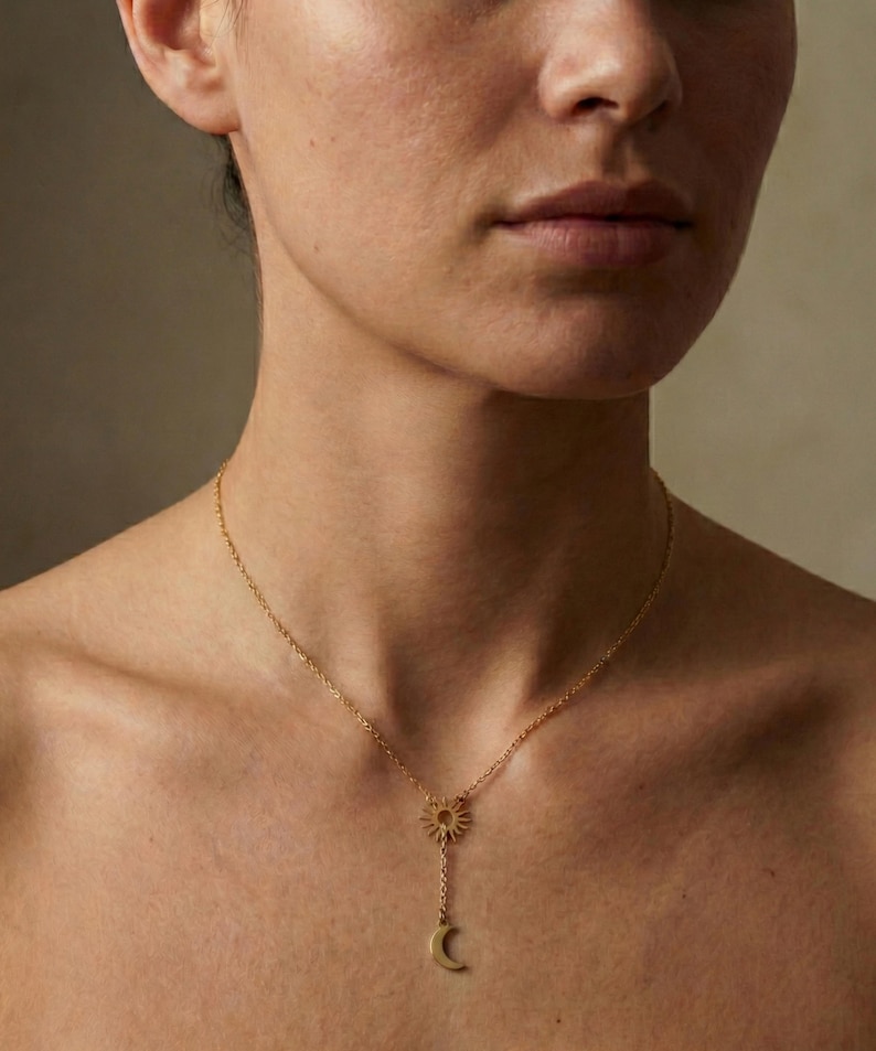 May include: A gold-colored necklace featuring a sun pendant at the top, with a chain extending down to a crescent moon charm. The necklace is worn around the neck, with the sun and moon pendants resting on the chest.