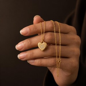 May include: A gold-toned necklace featuring a small heart-shaped pendant with the engraved text Love Mom. The pendant hangs from a delicate, thin gold-toned chain with a circular clasp visible, showcasing a polished metallic finish throughout.