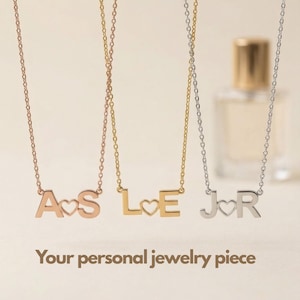 May include: Three delicate necklaces with metal chains, each featuring two capital letters separated by a small heart cutout. The letters are rose gold, yellow gold, and silver. The text "Your personal jewelry piece" is printed below the necklaces.