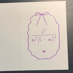 Peut inclure: Carte de vœux blanche ouverte, révélant un motif violet sur le côté droit. Le motif comprend une formule mathématique dans un cadre décoratif, surmonté d'un nœud et d'un petit cœur.
