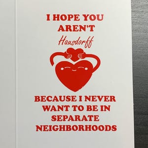以下が含まれることがあります： 赤い文字と赤いハートのグラフィックが入った白いグリーティングカード。テキストには「I HOPE YOU AREN'T Hausdorff BECAUSE I NEVER WANT TO BE IN SEPARATE NEIGHBORHOODS」と書かれています。