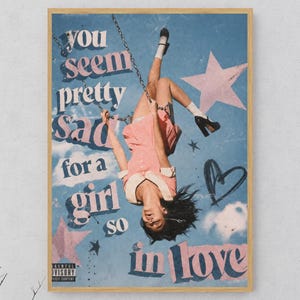 May include: A rectangular wall art print featuring a person in a pink dress hanging upside down from a swing against a blue sky background. The text reads you seem pretty sad for a girl so in love. Pink stars and a black heart graphic are included.