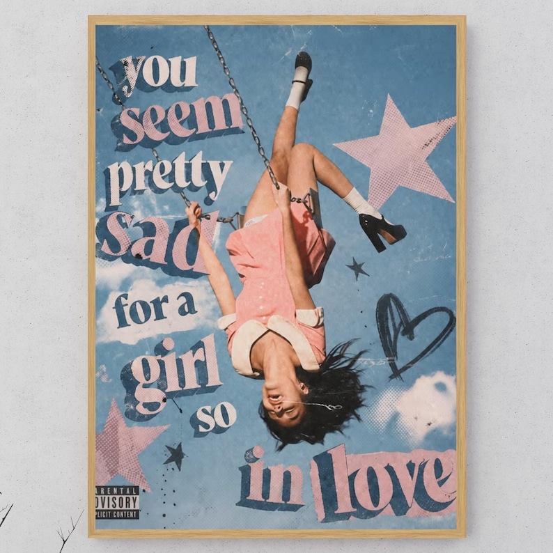 May include: A rectangular wall art print featuring a person in a pink dress hanging upside down from a swing against a blue sky background. The text reads you seem pretty sad for a girl so in love. Pink stars and a black heart graphic are included.