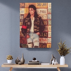 May include: A poster featuring a person with long dark hair wearing a black leather jacket with metallic accents, a white shirt, and light blue distressed jeans. The background is a collage of various colorful vintage American license plates.