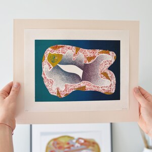 May include: Abstract art print featuring a colorful, organic shape with red, white, and gold accents against a teal and blue background. The artwork is displayed in a light beige mat.