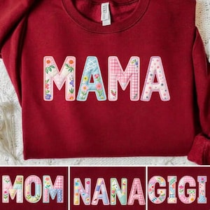 May include: A maroon sweatshirt with the word "MAMA" appliqued across the front. The letters are white with floral, gingham, and polka dot patterns. Below are three additional sweatshirts with the words "MOM", "NANA", and "GIGI".