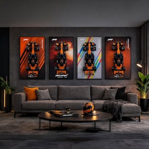 Könnte beinhalten: Vier gerahmte Poster von McLaren Formel-1-Autos. Jedes Poster zeigt eine Draufsicht auf das orange-schwarze Auto. Die Poster hängen über einem grauen Sofa mit orangefarbenen Kissen. Vorne steht ein Couchtisch mit Helm und Dekoration.