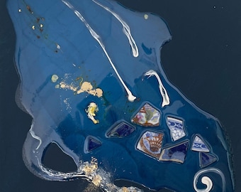 May include: A square canvas featuring a dark blue background with a central abstract resin pour in shades of blue. The design incorporates embedded fragments of blue and white patterned ceramic shards, gold leaf flakes, and white swirling lines.