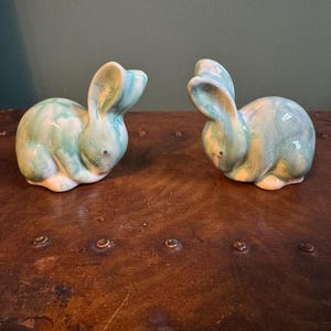 Könnte beinhalten: Zwei Keramik-Hasenfiguren mit einer marmorierten grün-blauen Glasur. Die Hasen sitzen mit aufgestellten Ohren. Die Figuren sind dekorativ und eignen sich für die Oster- oder Frühlingsdekoration.