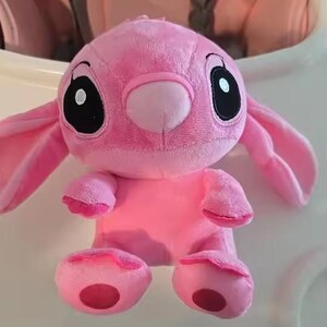Puede incluir: Un peluche rosa con un personaje de orejas grandes, ojos negros y nariz redonda. El juguete tiene una textura suave y difusa y est&aacute; sobre una superficie blanca. Tambi&eacute;n son visibles los brazos y los pies del juguete.