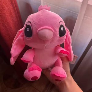 Puede incluir: Un peluche rosa de un personaje de dibujos animados con grandes ojos negros, orejas largas y una peque&ntilde;a antena. El juguete tiene una textura suave y difusa.
