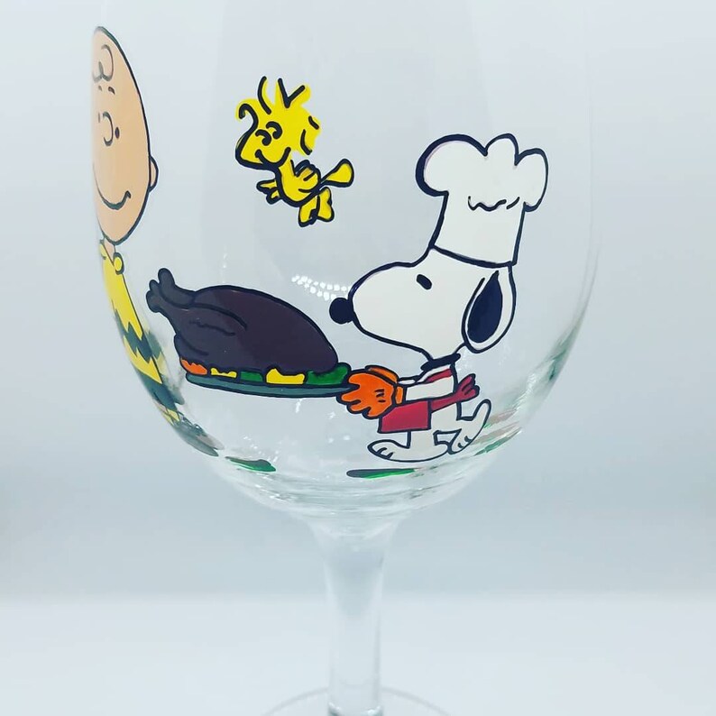 Pode incluir: Uma ta&ccedil;a de vinho de vidro transparente com um design pintado &agrave; m&atilde;o que apresenta Snoopy, Woodstock e Charlie Brown. Snoopy est&aacute; vestido de cozinheiro e segura uma bandeja com um peru assado. A ta&ccedil;a &eacute; perfeita para servir vinho ou outras bebidas.
