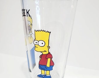 May include: A clear glass with a cartoon image of Bart Simpson and Homer Simpson from the Simpsons television show. The glass has the word "BEIK" written on it.