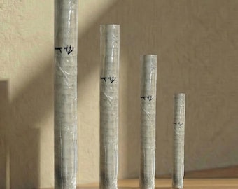 May include: Five gray cylindrical objects of varying heights, wrapped in clear plastic, stand on a wooden shelf. Each cylinder has a black Hebrew symbol. The shelf is made of light brown wood, and the background is a beige wall.