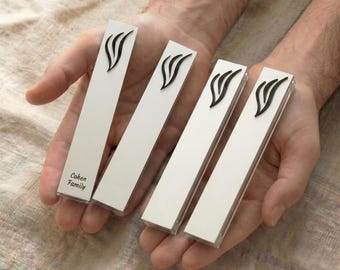 May include: Four white rectangular objects with a black decorative design are held in open hands. The objects have a clear plastic casing. The text "Cohen Family" is printed on one of the objects.