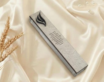 May include: A rectangular, clear glass mezuzah case with a light gray textured front and dark gray trim. A black flame design is at the top, and Hebrew text is printed vertically down the front.