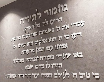 May include: Silver metallic Hebrew text is affixed to a gray wall. The text is a psalm of thanksgiving, with multiple lines of script. The wall has a textured appearance.