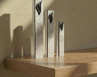 May include: Three clear acrylic awards with a textured, light gray center panel. Each award features a black flame design at the top and text in Hebrew. The awards are displayed on a wooden shelf.