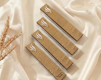 May include: Four rectangular wooden boxes with a light brown finish, each featuring a white, stylized flame design. The boxes are arranged on a cream-colored satin surface. The bottom box has the text "Rosenberg Family".
