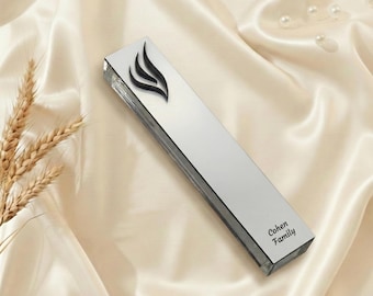 May include: A rectangular, mirrored mezuzah case with a black flame design. The text "Cohen Family" is printed on the bottom. The case is displayed on a cream-colored satin fabric.