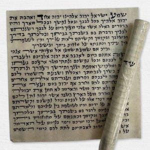 Op de afbeelding: Een opgerolde perkamentrol met Hebreeuwse tekst, gedeeltelijk uitgerold, en een vel papier met dezelfde tekst. De tekst is in zwarte inkt op verouderd papier. De rol is verpakt in doorzichtig plastic.