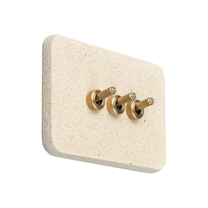 Peut inclure: Une plaque d'interrupteur rectangulaire beige clair avec trois interrupteurs à bascule en laiton. La plaque a une surface texturée et des coins arrondis. Les bascules en laiton sont cylindriques avec une poignée moletée.