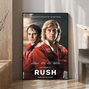 Pode incluir: Pôster emoldurado do filme "Rush" com Chris Hemsworth e Daniel Brühl em macacões de corrida vermelhos. O pôster inclui o título do filme e o slogan "Everyone's Driven by Something."