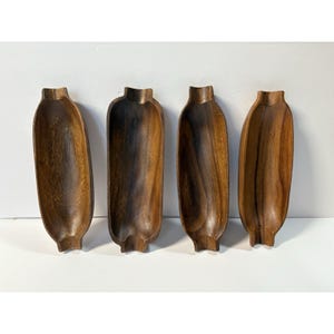 May include: Four wooden serving bowls with a dark brown finish. Each bowl has a unique shape, resembling a corn cob. The bowls are made of a dark wood and are arranged in a row against a white background.