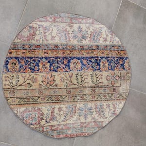 Könnte beinhalten: Ein runder Teppich im Vintage-Stil mit einem verblichenen, abgenutzten Aussehen. Der Teppich hat ein Patchwork-Design mit verschiedenen Mustern und Farben, darunter Beige, Blau, Rot und Braun. Der Durchmesser des Teppichs beträgt ca. 122 cm.