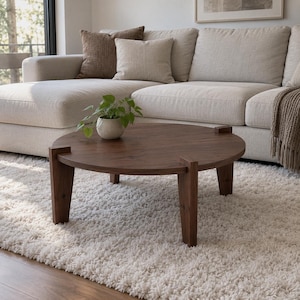 May include: A round, dark brown wooden coffee table with four thick, straight legs that extend slightly above the tabletop surface. A small, green potted plant in a light-colored, speckled ceramic pot sits on the center of the table.
