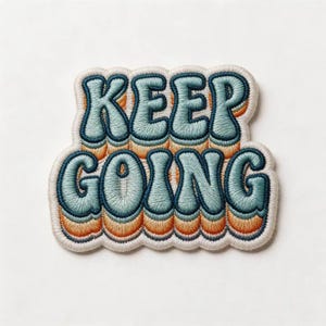 May include: An embroidered patch featuring the text KEEP GOING in a bold, rounded font. The letters are light blue with dark blue outlines, layered over a gradient of orange and yellow tones, all bordered by a thick, cream-colored stitched edge.