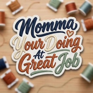 May include: A white fabric patch with embroidered text that reads Momma Your Doing At Great Job in dark blue, light beige, rust orange, and sage green thread. The design features a small embroidered heart and a scalloped edge finish.
