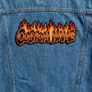 May include: A denim jacket with a custom patch. The patch features the text "CUSTOM NAME" in a flame design with red, orange, and yellow colors. The patch is outlined in black and has a black border.