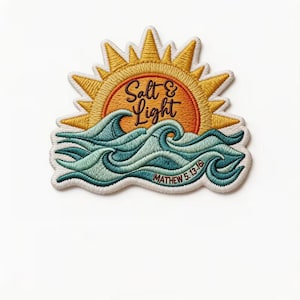May include: An embroidered patch featuring a yellow sun rising over teal and blue ocean waves. The text Salt & Light is stitched in black in the center of the sun, with the text MATHEW 5.13-16 stitched in black along the bottom wave edge.