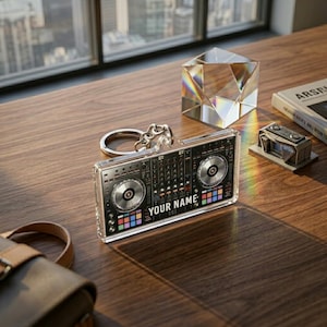 May include: A rectangular acrylic keychain featuring a detailed graphic print of a DJ mixing console with two circular platters, colorful buttons, and the text YOUR NAME printed in white across the center, attached to a silver metal ring.