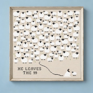 May include: A framed cross-stitch artwork on beige fabric featuring a large group of white sheep with black faces and legs. Below the sheep, the text HE LEAVES THE 99 is stitched in black, with a line connecting to a figure and one small sheep.