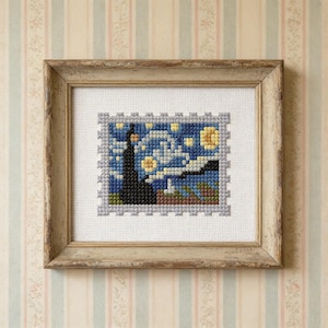 May include: A framed cross-stitch depicting Van Gogh's "Starry Night." The artwork features a dark, silhouetted church steeple and rolling hills under a swirling blue sky filled with yellow stars. The frame is a distressed, light brown color.