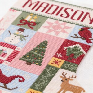 以下が含まれることがあります： 赤色で「MADISON」と刺繍されたパーソナライズされたクリスマスストッキング。雪だるま、クリスマスツリー、トナカイなどのお祝いのイメージが、赤、緑、ピンク、青の色合いでパッチワークデザインに施されています。